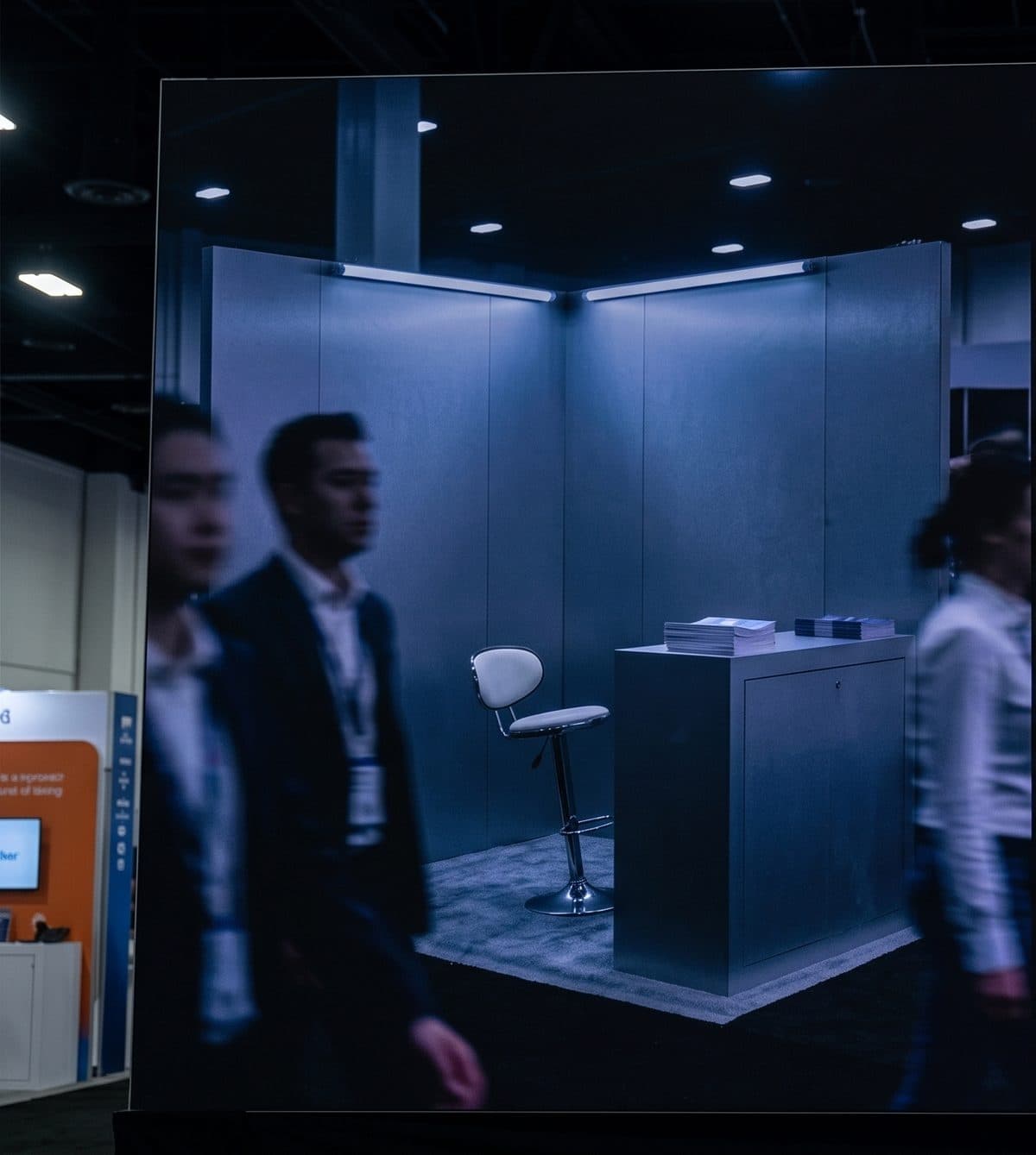 A deserted conference booth: empty chairs, an unattended counter, and a handful of attendees walking straight past.